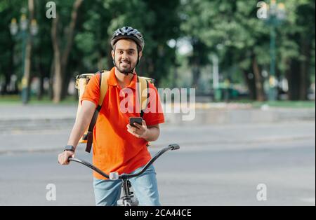 Cycliste avec administration. Happy Courier avec sac à dos, montre intelligente et smartphone, assis sur un vélo Banque D'Images