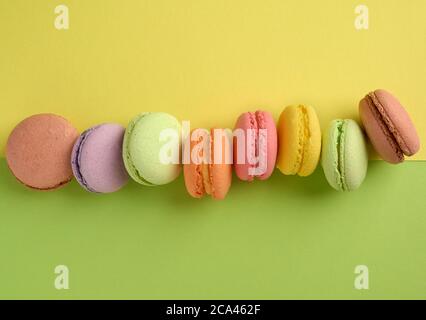 les biscuits macarons multicolores cuits se trouvent dans une rangée sur un fond jaune-vert, vue de dessus Banque D'Images