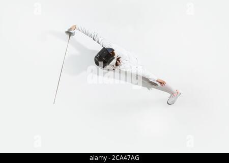 D'abord. Jeune fille en costume d'escrime avec épée à la main sur fond blanc. Vue de dessus. Jeune femme modèle pratique et formation en mouvement, action. CopySpace. Sport, jeunesse, mode de vie sain. Banque D'Images