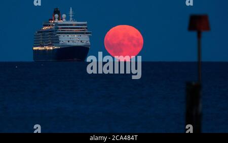 Bournemouth, Royaume-Uni. 3 août 2020. La pleine lune d'août, parfois connue sous le nom de Sturgeon Moon, s'élève derrière le navire de croisière Cunard Line Queen Elizabeth à l'ancre dans la baie Poole, au large de la plage de Bournemouth. Credit: Richard Crease/Alay Live News Banque D'Images