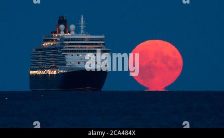 Bournemouth, Royaume-Uni. 3 août 2020. La pleine lune d'août, parfois connue sous le nom de Sturgeon Moon, s'élève derrière le navire de croisière Cunard Line Queen Elizabeth à l'ancre dans la baie Poole, au large de la plage de Bournemouth. Credit: Richard Crease/Alay Live News Banque D'Images