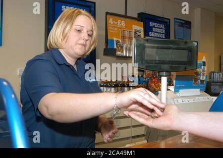 Jeune femme travaillant dans la boutique de location de vidéos Blockbuster au service d'un client; Merseyside Banque D'Images