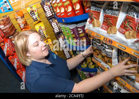 Jeune femme travaillant dans la boutique de location de vidéos Blockbuster ; organisation des étagères de chips ; Merseyside Banque D'Images