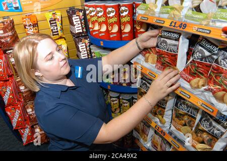 Jeune femme travaillant dans la boutique de location de vidéos Blockbuster organisant l'exposition de chips à vendre; Merseyside Banque D'Images