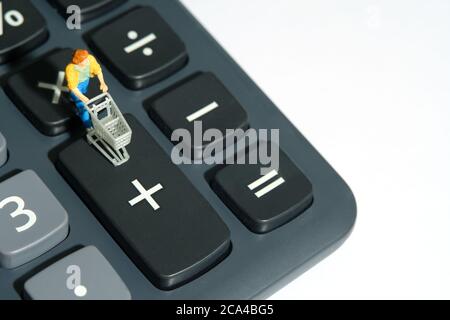 Femme avec le panier debout sur la calculatrice, calcul de l'achat total pour le shopping. Miniature personnes figurines jouets photographie conceptuelle. Banque D'Images