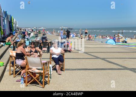 Des amis s'assoient sur des chaises sur la promenade au bord de la belle plage de sable de Southwold. Il fait très chaud et beaucoup de gens apprécient l'été anglais. Certaines personnes essaient de garder la distance sociale à cause de l'épidémie de Covid, d'autres pas. Le quai se trouve en arrière-plan. Banque D'Images