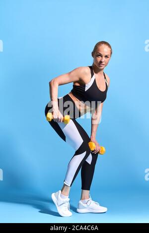 femme mince et motivée qui fait assis, arrière-plan bleu isolé, prise de vue en studio, photo pleine longueur. bien-être, bien-être. Banque D'Images