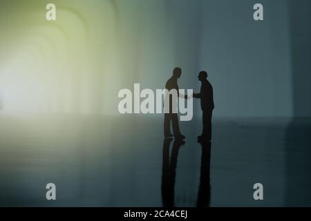 La silhouette de deux hommes d’affaires est un accord de partenariat poignée de main. Les personnes miniatures se font une photographie conceptuelle Banque D'Images