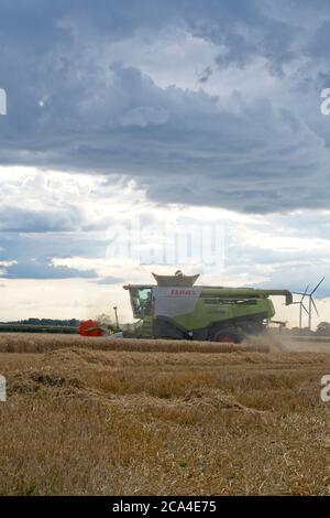 Récolte d'hiver vue latérale sur la distance moyenne de la moissonneuse-batteuse combinée Travail dans le champ récolte de récolte ciel nuageux poussière voler Portrait format Banque D'Images