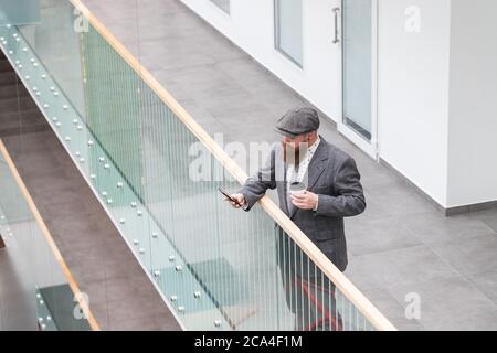 Homme d'affaires à barbe brutale portant un blazer en laine, cachez le café d'une tasse en papier, en utilisant un smartphone. Il est temps de faire une pause. Une pause pendant le travail. Haut Banque D'Images