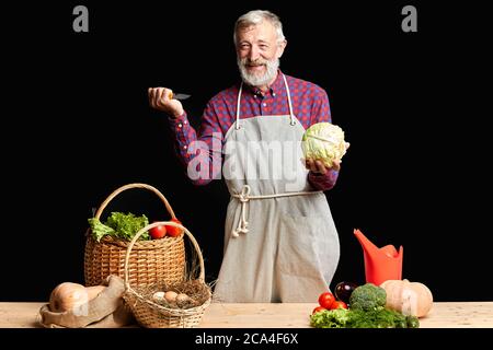 Beau homme mûr dans le nettoyage de tablier, la coupe, hacher des légumes crus biologiques de la ferme locale, prenant part à la classe de maître de cuisine, faisant saine d Banque D'Images