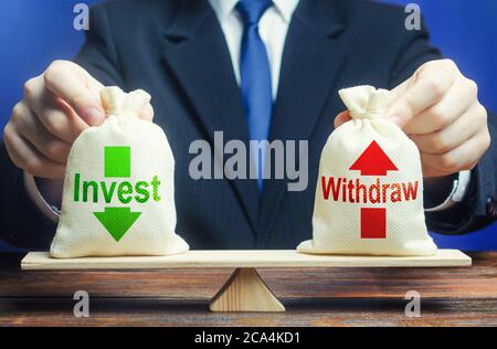 Homme d'affaires tient des sacs investir et se retirer sur des balances. Gestion des bénéfices d'entreprise. Investir dans l'économie nationale d'une entreprise, ou retirer des fonds à la maison Banque D'Images