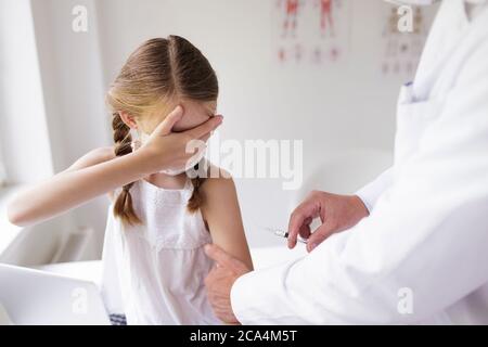 Médecin avec masque buccal donne l'injection à la fille avec masque buccal Banque D'Images