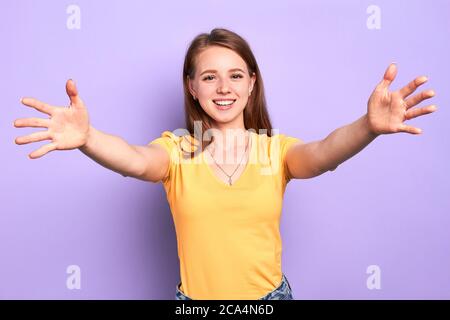 Bonne adolescente fille montre geste de bienvenue, se répand les mains, montre les palmiers, veut câliner et câliner meilleur ami qu'elle n'a pas vu pendant longtemps, sourire Banque D'Images