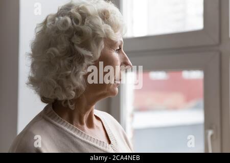 Une femme âgée pensive qui regarde la fenêtre attend se sent seule Banque D'Images