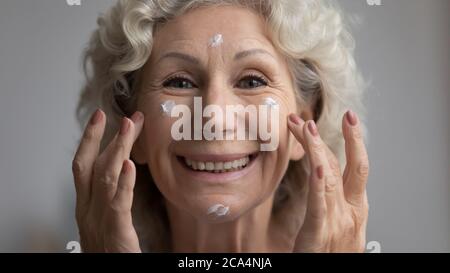 Gros plan la femme âgée appliquant une crème efficace pour le visage se sent heureuse Banque D'Images