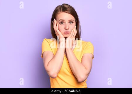 Stupéfied triste fille garde les mains sur son visage, regarde avec l'expression bouleversée dans la caméra, a embarrassé et l'expression contemplative, reçu désagréable n Banque D'Images