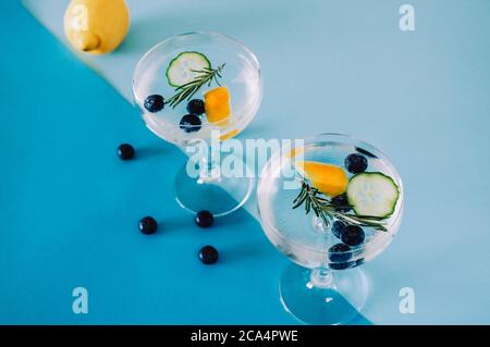Deux verres de gin et de boisson tonique pour cocktail avec bleuets, concombres et romarin isolés sur fond bleu abstrait et géométrique Banque D'Images