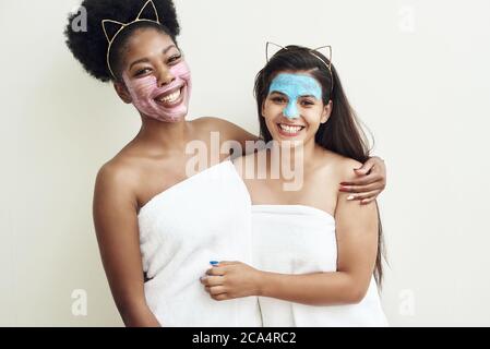 Jeune belle femme noire et son adorable ami souriant, embrassant dans des masques hydratants et anti-âge. Fin des soins de la peau à la maison, les amies et l'amour. Banque D'Images