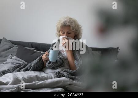 Une femme âgée malsaine soufflant le nez s'asseyant dans le lit Banque D'Images