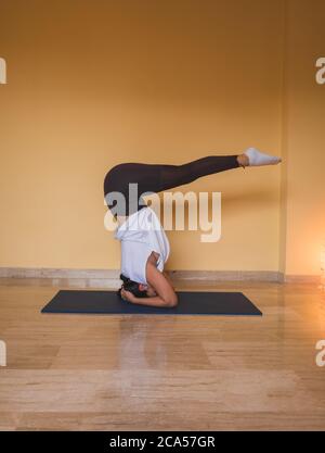 femme anonyme commençant la posture prise en charge de la tête de lit. Vue latérale d'une femme mince faisant du yoga dans un salon confortable pendant la journée à la maison. Banque D'Images