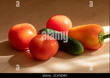 Concombre mûr, tomates juteuses et poivrons doux sur une table en bois clair au soleil. Gros plan Banque D'Images