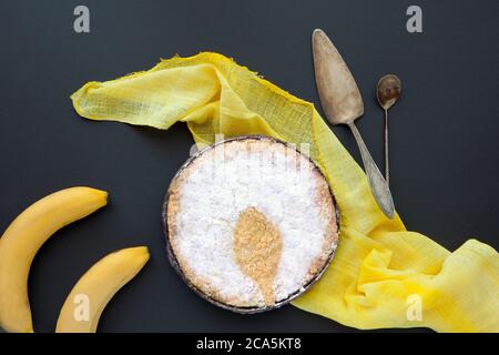 Gâteau de banane sur fond noir avec couverture jaune et cuillères à café. Tarte maison sur fond sombre et ombre à la cuillère Banque D'Images