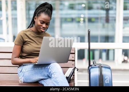 Jeune femme africaine avec des bagages à main dans le terminal de l'aéroport, travaillant sur son ordinateur portable en attendant le vol Banque D'Images