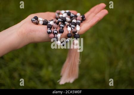 Main femelle tenant un japa bouddhiste mala fait de 108 perles de pierres naturelles pour la méditation sur fond d'herbe verte Banque D'Images
