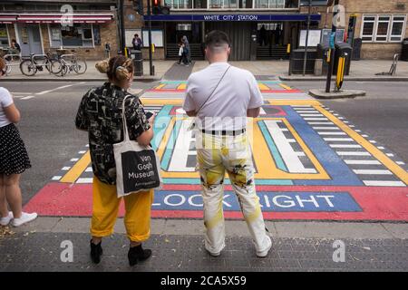 Un couple attend à côté des passages géométriques pour piétons de l'artiste français Camille Walala devant la station de métro White City à l'ouest de Londres, Royaume-Uni Banque D'Images