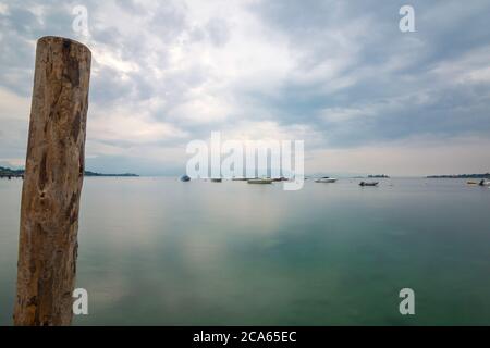 Vue sur le lac de Garde en début de matinée ou en soirée. L'eau est calme, le ciel est partiellement nuageux. Les petits bateaux dansent sur l'eau. L'humeur est rêveuse. Banque D'Images