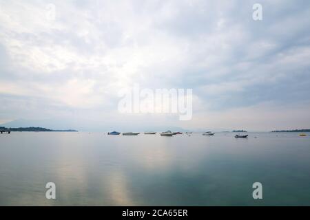 Vue sur le lac de Garde en début de matinée ou en soirée. L'eau est calme, le ciel est partiellement nuageux. Les petits bateaux dansent sur l'eau. L'humeur est rêveuse. Banque D'Images