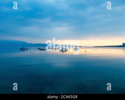 Vue sur le lac de Garde en début de matinée ou en soirée. L'eau est calme, le ciel est partiellement nuageux. Les petits bateaux dansent sur l'eau. L'humeur est rêveuse. Banque D'Images