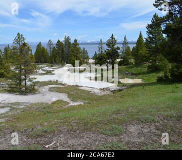 Fin du printemps dans le parc national de Yellowstone : pots de peinture au pouce dans le bassin West Thumb Geyser sur la rive du lac Yellowstone avec la chaîne d'Absaroka au-delà Banque D'Images