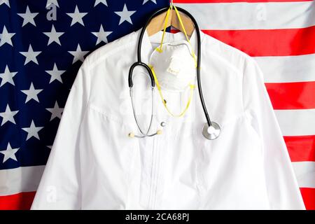 Le Doctor's est équipé d'un stéthoscope et d'un masque médical sur le support. Le manteau du médecin sur fond de drapeau américain. Coronavirus, covid-19, copyspace, medicaltemplat Banque D'Images