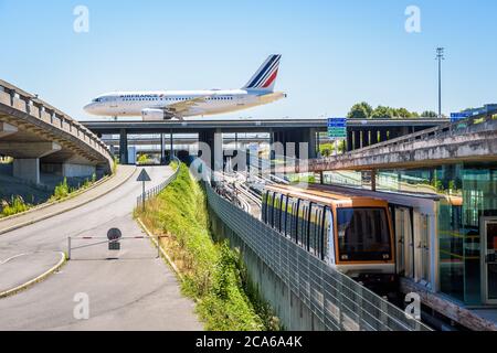 Un avion de ligne roule sur un pont de taxi de l'aéroport Paris-Charles de Gaulle tandis qu'une navette CDGVAL stationne à la gare du terminal 1. Banque D'Images