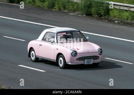 Une voiture Nissan Figaro Pink car Cabriolet essence 2011 conduite sur l'autoroute M6 près de Preston dans Lancashire, Royaume-Uni Banque D'Images