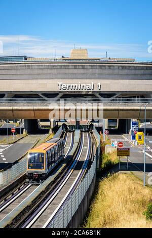 Une navette de l'aéroport CDGVAL quitte le bâtiment circulaire en béton du terminal 1 de l'aéroport Paris-Charles de Gaulle par une journée ensoleillée. Banque D'Images