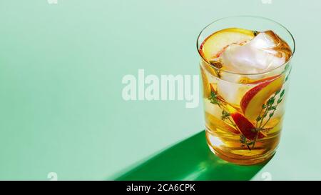 Pétillant et froid, thé de pêche au thym dans un verre sur fond de papier vert, gros plan. Concept de boissons rafraîchissantes sans alcool en été Banque D'Images