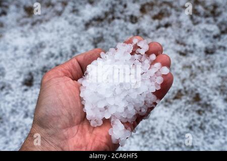 Vue rapprochée de la paume gauche pleine de pierres de grêle. La main gèle de la glace froide et devient humide et rouge de la fonte des boules de grêle Banque D'Images