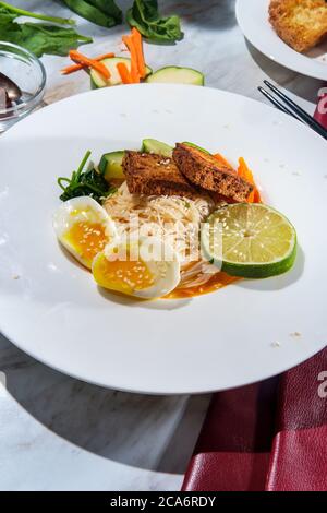 Soupe thaïlandaise de nouilles de riz au curry rouge accompagnée de tofu frits croustillants et d'œufs durs Banque D'Images