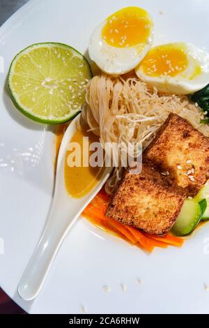 Soupe thaïlandaise de nouilles de riz au curry rouge accompagnée de tofu frits croustillants et d'œufs durs Banque D'Images