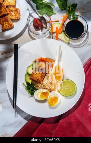 Soupe thaïlandaise de nouilles de riz au curry rouge accompagnée de tofu frits croustillants et d'œufs durs Banque D'Images