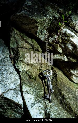 Anciennes clés à squelette accrochées à une chaîne métallique contre un mur de roche en mousse Banque D'Images