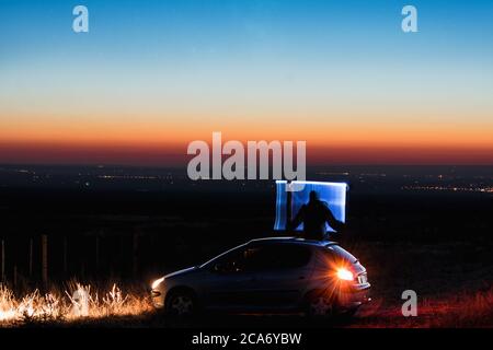 jeune homme assis sur la voiture avec un faisceau lumineux de peinture légère dans ses mains un Banque D'Images