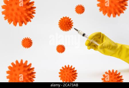 Concept de recherche et de test d'un vaccin contre le coronavirus, Covid-19. Une main dans un gant de protection jaune insère une injection dans un modèle de coronavirus Banque D'Images