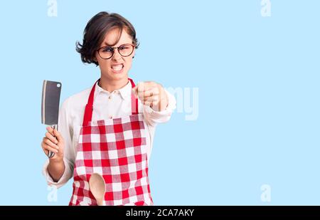 Belle jeune femme aux cheveux courts portant un tablier professionnel de boulanger tenant le couteau agacé et frustré criant avec colère, hurlant fou avec un Banque D'Images