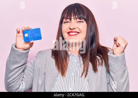 Jeune femme de taille plus tenant la carte de crédit criant fier, célébrant la victoire et le succès très excité avec le bras levé Banque D'Images