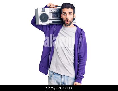 Jeune homme beau avec barbe écoutant de la musique avec boombox vintage effrayé et stupéfié avec la bouche ouverte pour la surprise, le visage incrédulé Banque D'Images