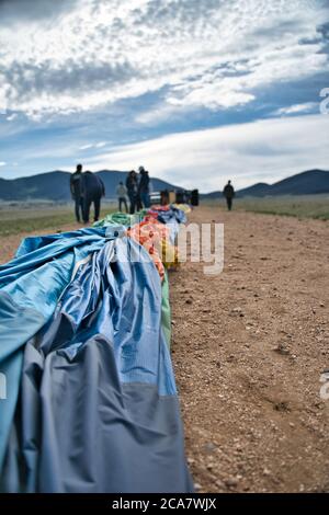 Ballon d'air chaud dégonflé sur route poussiéreuse. Les gens et les montagnes visibles au loin. Banque D'Images